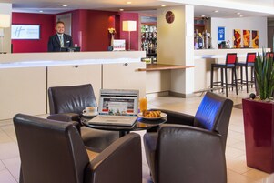 Un vestíbulo de hotel con una recepción, zona de estar con sillones de cuero, una computadora portátil sobre una mesa y un bar al fondo.