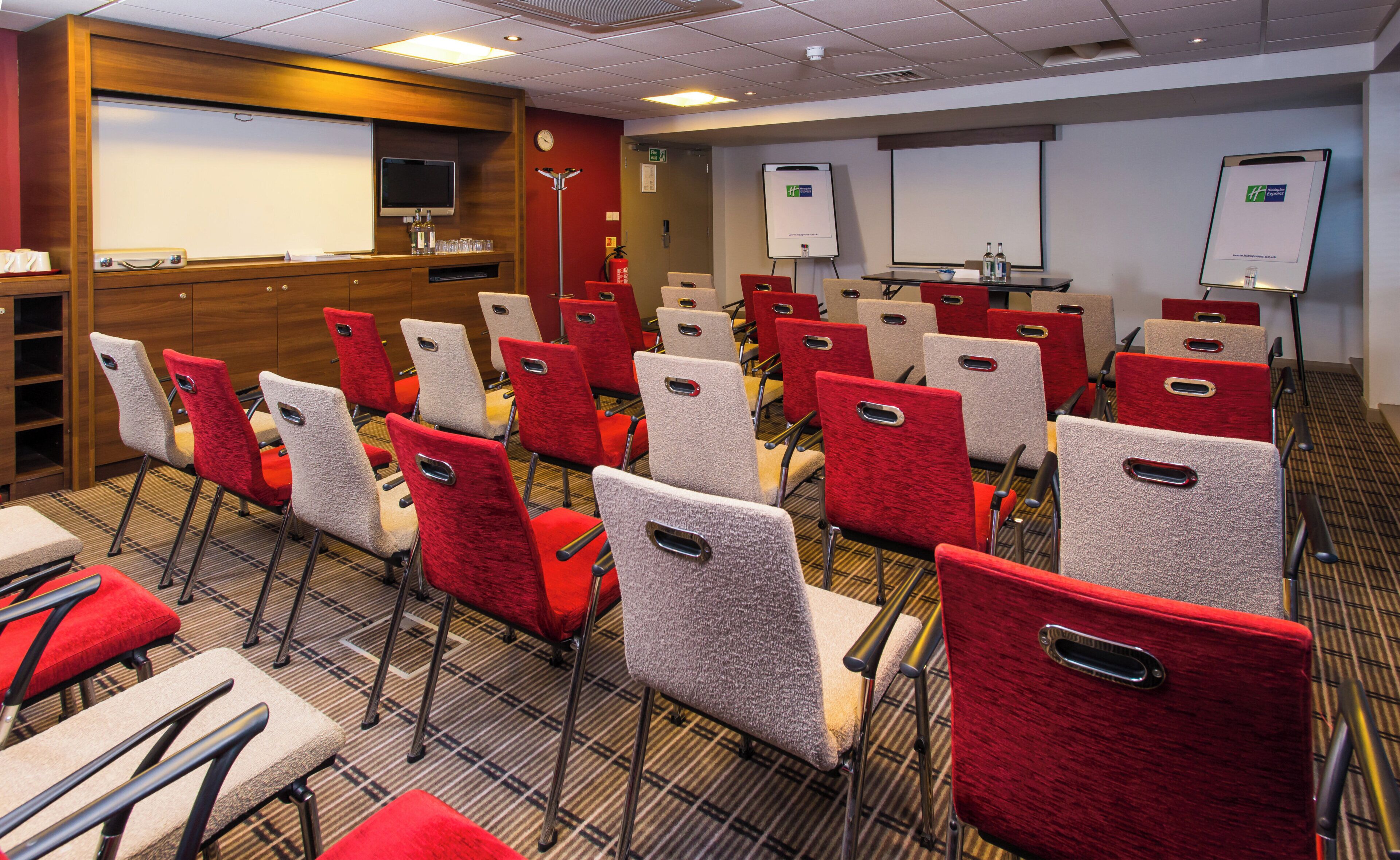 A conference room with rows of chairs, a whiteboard, and a projector screen.