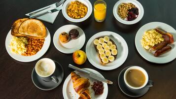 Una mesa de desayuno con diversos platos, incluyendo tostadas, frijoles, muffins, plátanos, salchichas y café.
