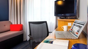 A hotel room with a sofa, a desk with a laptop, a chair, a TV, and a window with curtains. - Holiday Inn Express East Midlands Airport by IHG (Derby)