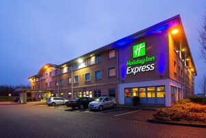 Edificio de Holiday Inn Express con estacionamiento y varios automóviles estacionados al frente.