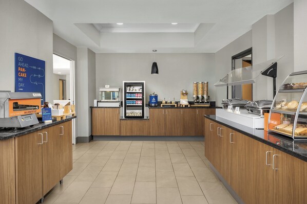 Una cucina moderna con un angolo colazione self-service, che include una macchina del caffè, un frigorifero e una vetrina con dolci.