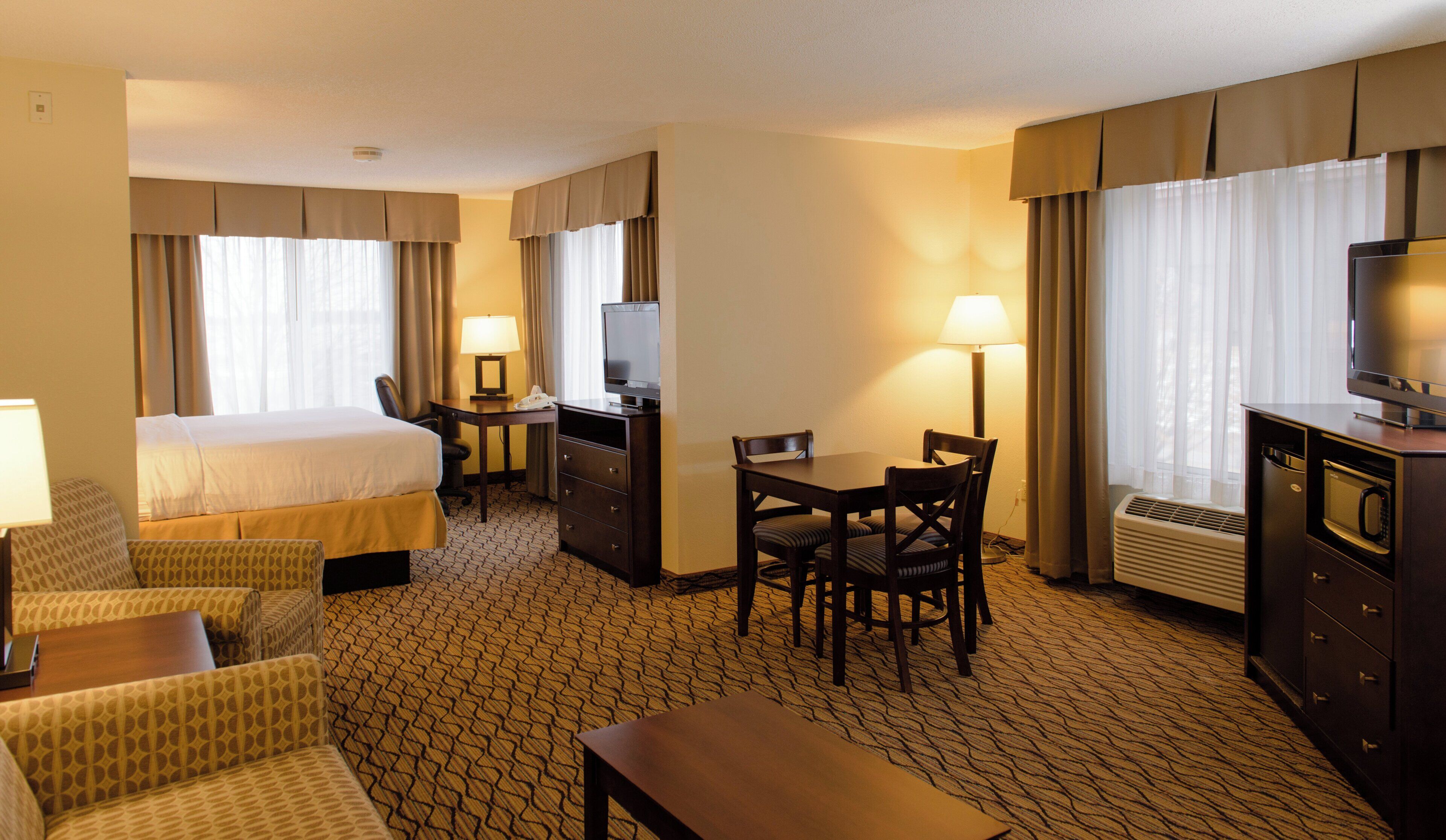 A hotel room with a bed, desk, chair, table, and a television.