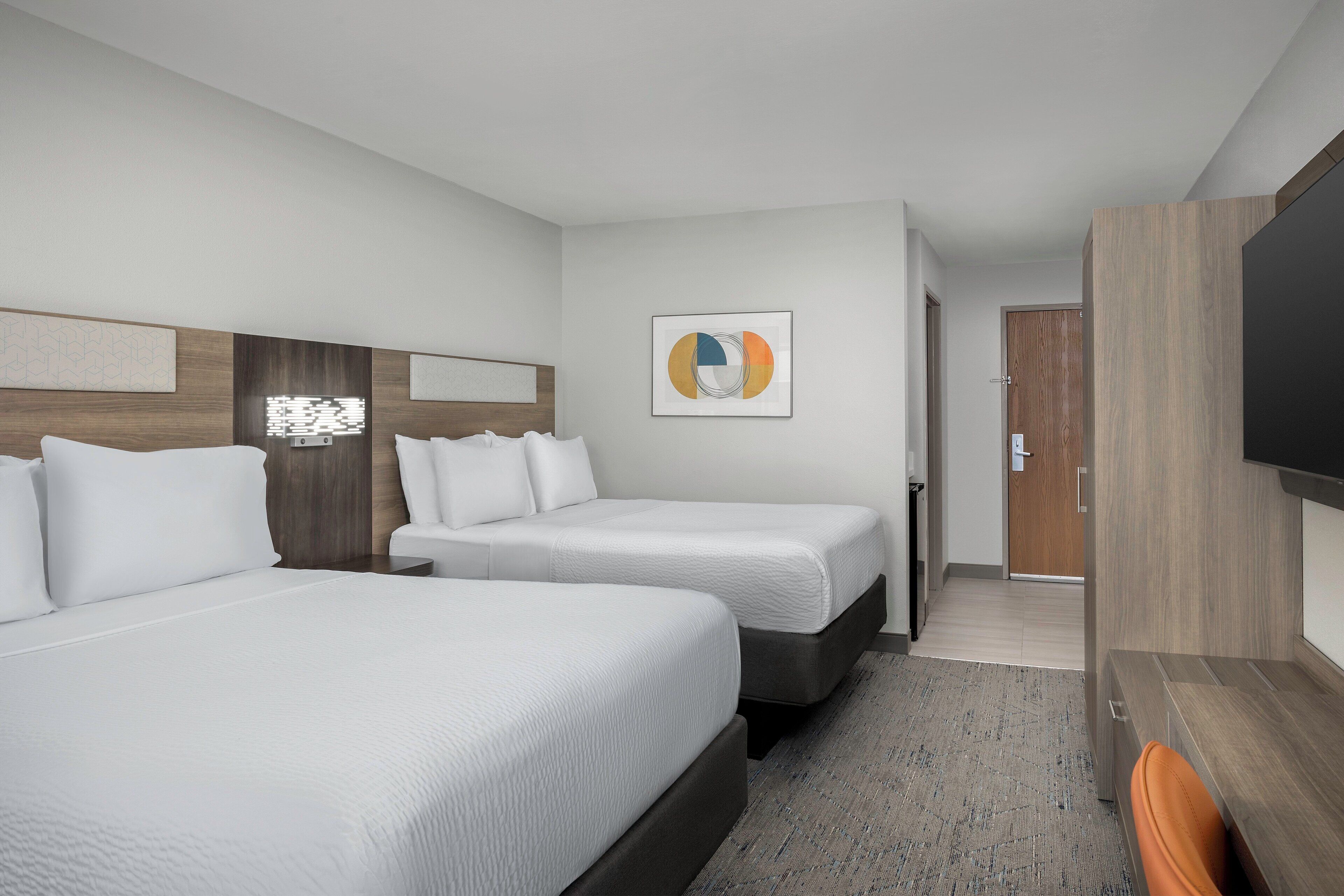 Een hotelkamer met twee bedden, een flatscreen televisie en een deur die naar een andere kamer leidt.