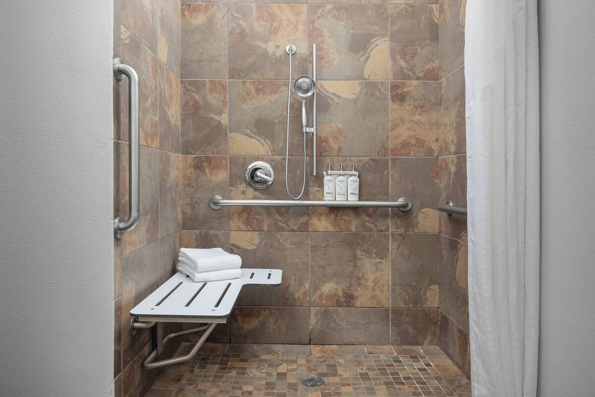 Un espace douche équipé d’une barre d’appui, d’une étagère pour les articles de toilette et d’un banc.