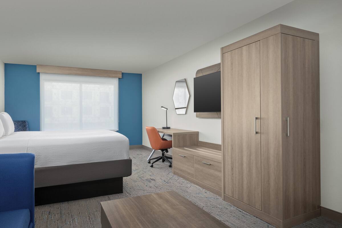 Une chambre d’hôtel équipée d’un lit, d’un bureau, d’une chaise, d’une armoire et d’un téléviseur fixé au mur.