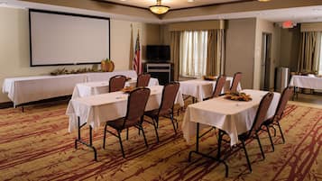 A conference room with tables, chairs, a projector screen, an American flag, and a television.