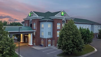 Experience the charm of this Holiday Inn Express hotel, featuring a brick facade, green roof, and beautifully landscaped surroundings.