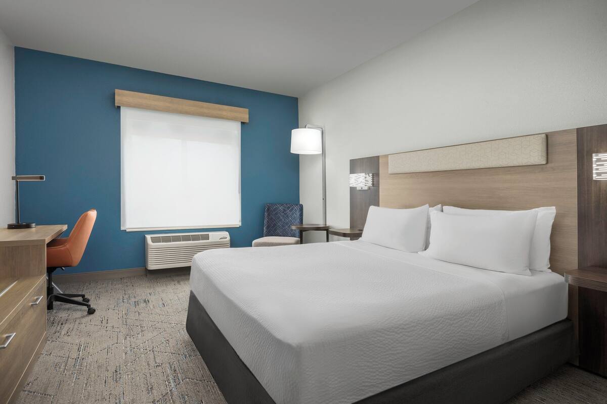 Une chambre d’hôtel avec un grand lit, un bureau, une chaise et une fenêtre avec des stores.