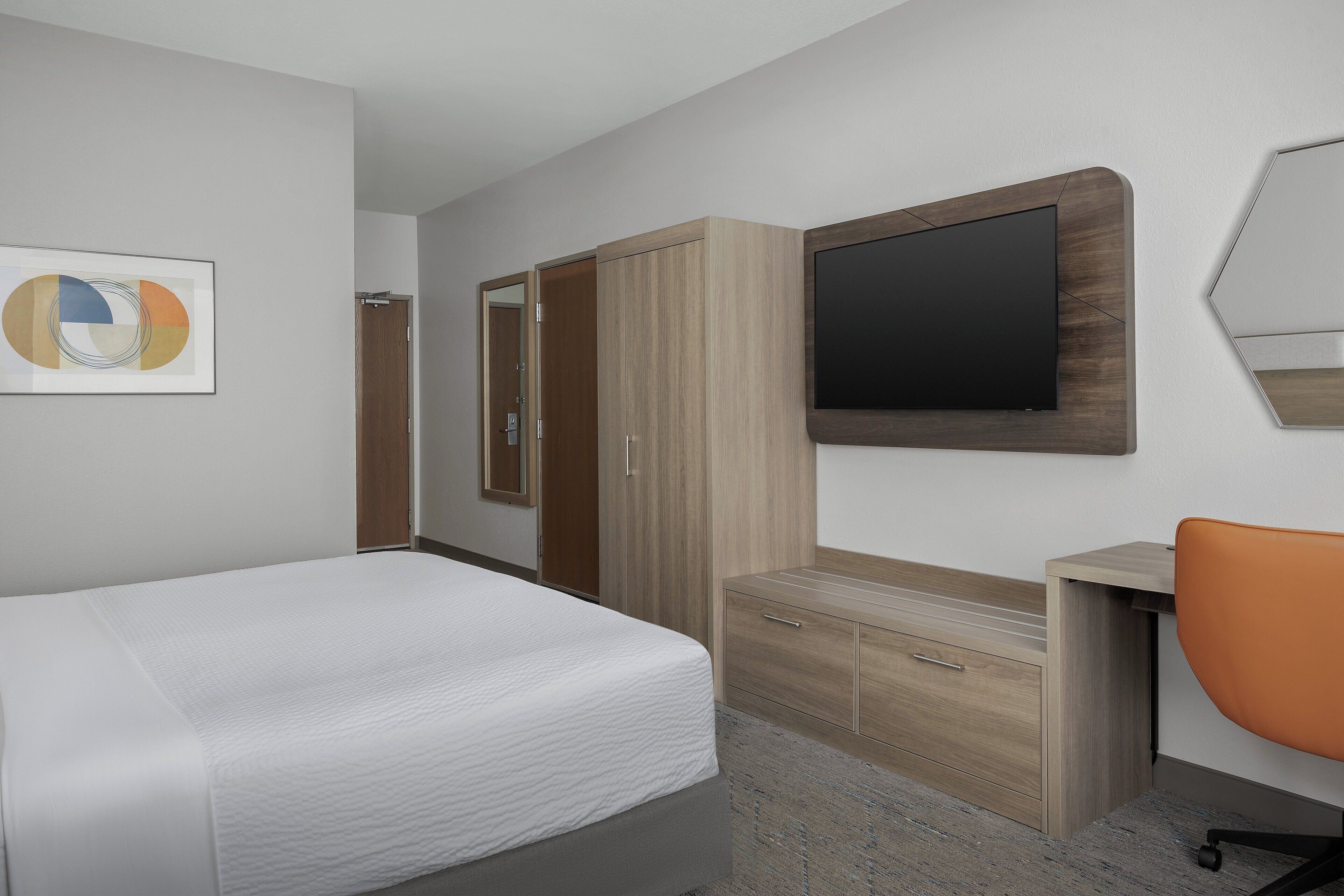 Una habitación de hotel con cama, escritorio, silla, armario y televisor.