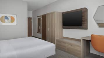 Una habitación de hotel con cama, escritorio, silla, armario y televisor.