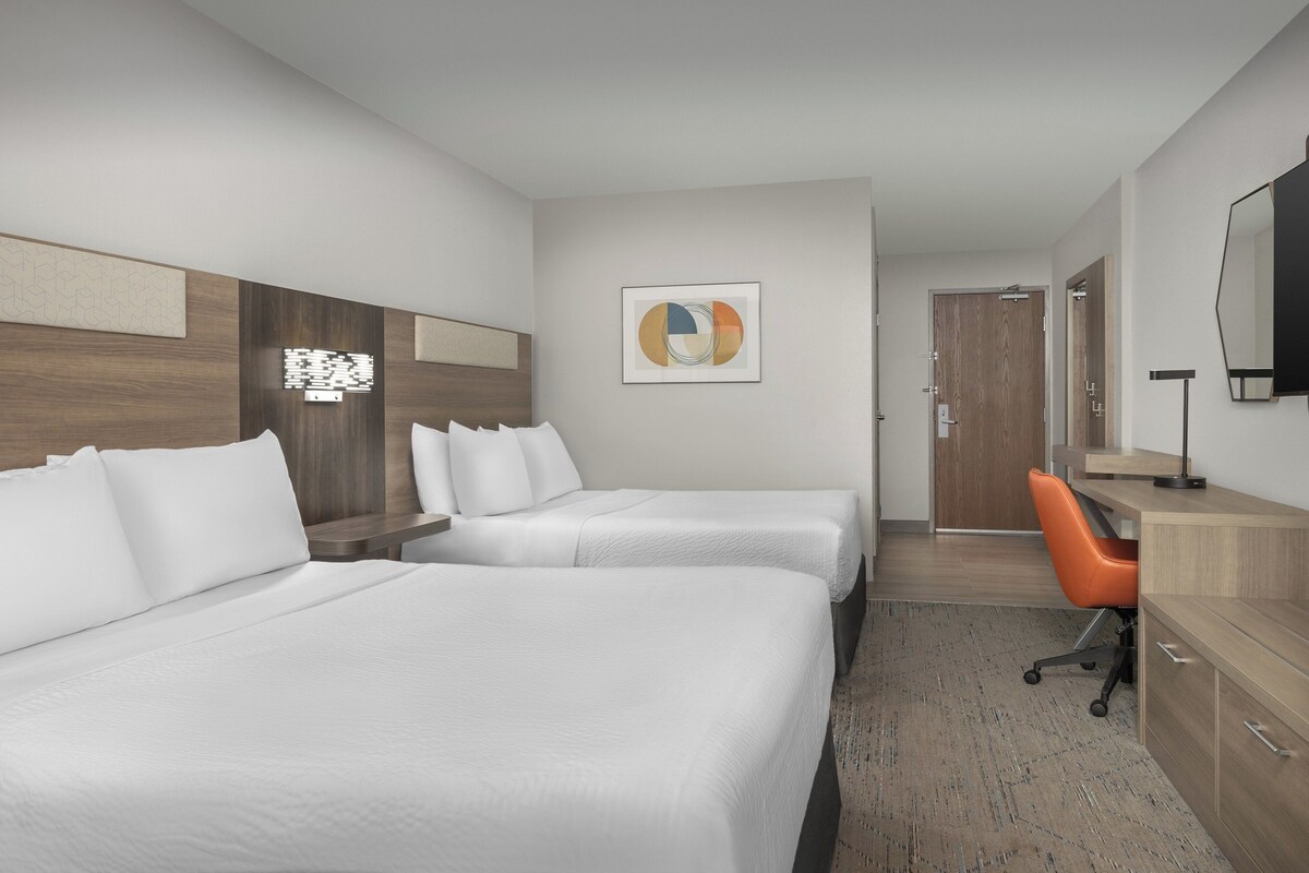 Quarto de hotel com duas camas, uma escrivaninha, uma cadeira e um espelho grande.