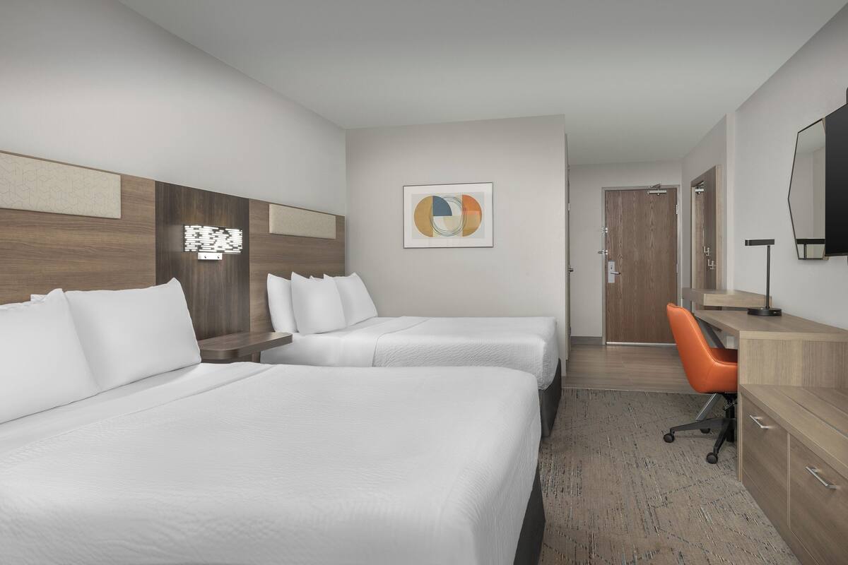 Une chambre d’hôtel avec deux lits, un bureau, une chaise et un grand miroir.