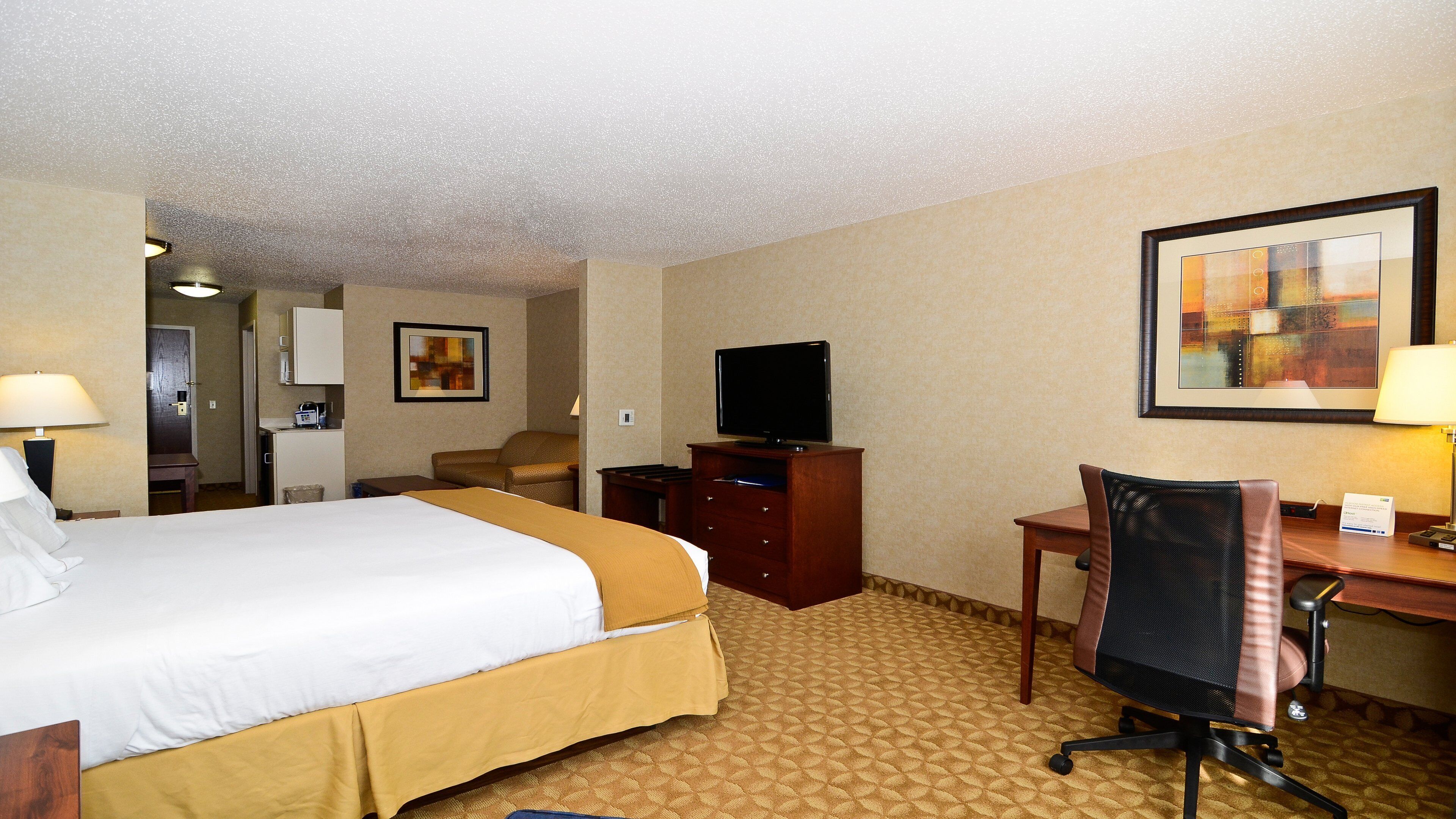 A hotel room with a bed, a desk, a chair, a television, and a painting on the wall.