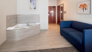 A modern bathroom with a large bathtub, a blue sofa, and a wooden floor.
