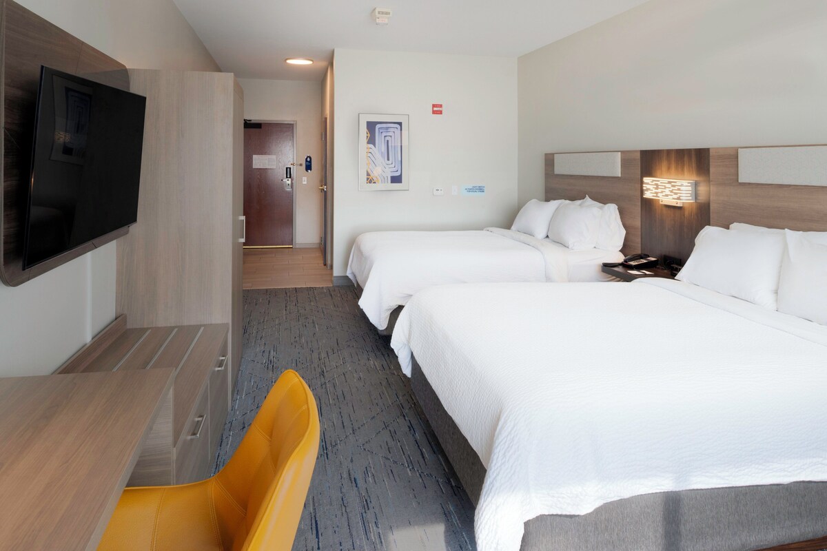 A hotel room with two beds, a TV mounted on the wall, a desk, and a chair.