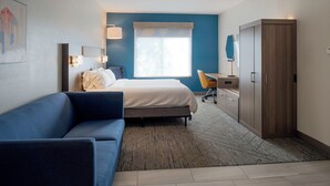 A modern hotel room with a bed, a blue sofa, a desk, and a wardrobe.