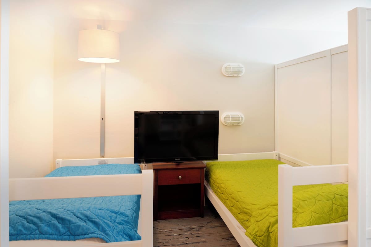 A room with two bunk beds, a television, a bedside table, and a lamp.