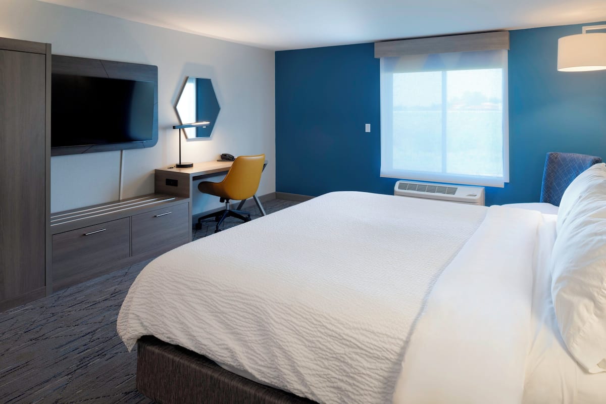 A hotel room with a bed, a desk, a chair, a TV, and a window.