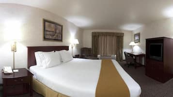 A hotel room with a large bed, a desk, a chair, a television, and a lamp.