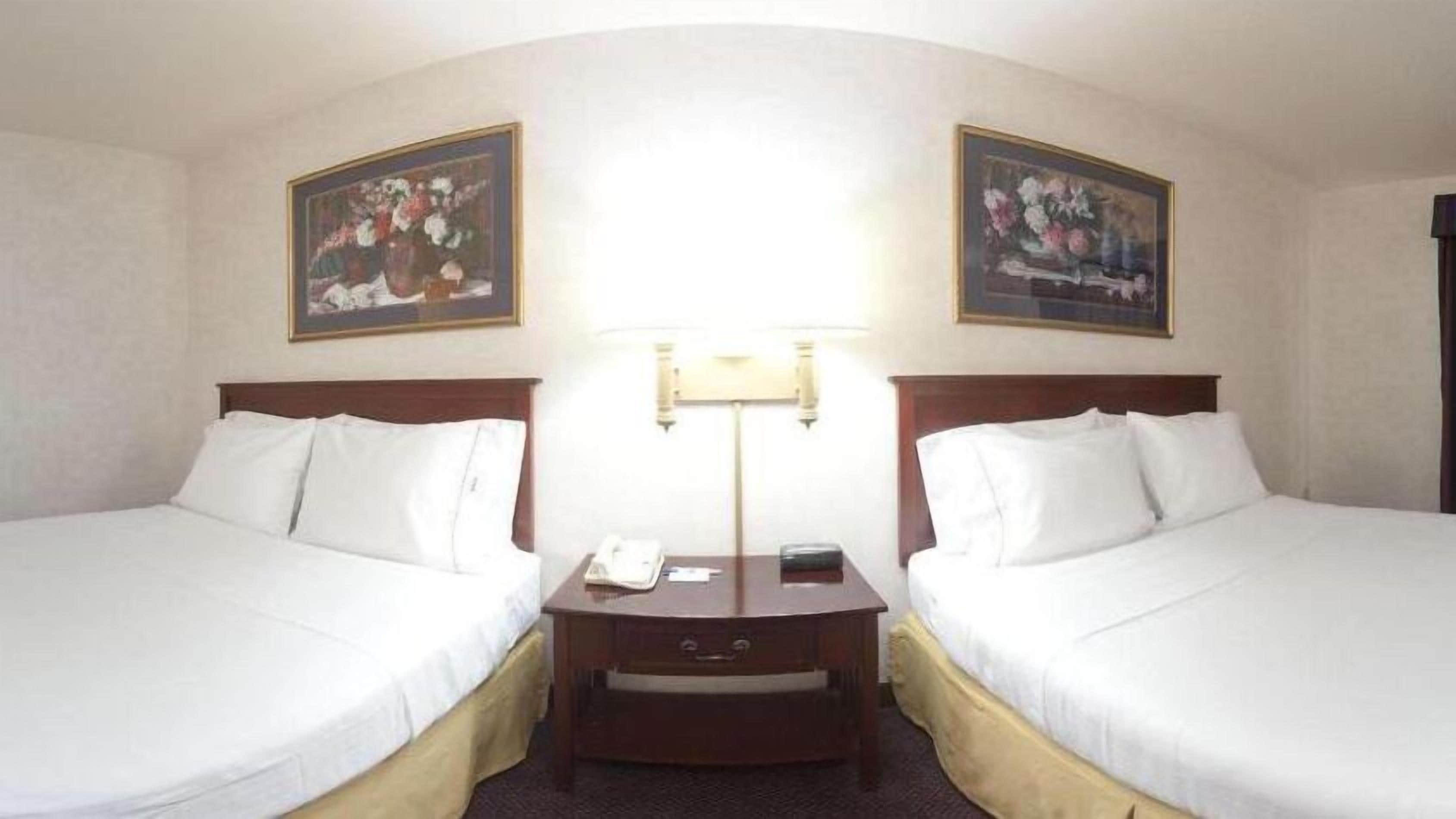 A hotel room with two single beds, a nightstand with a lamp, a phone, and a small drawer.
