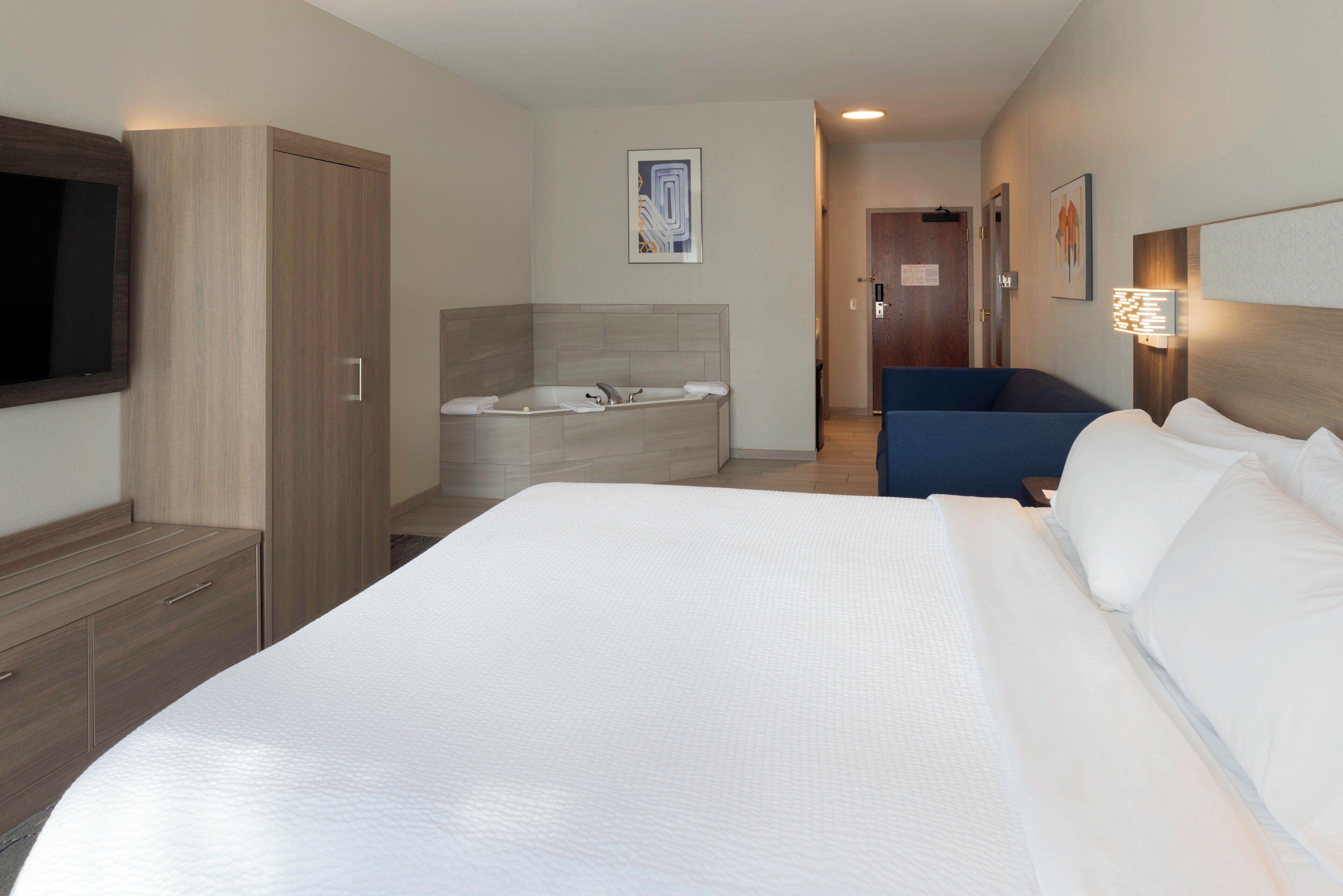A hotel room with a large bed, a sitting area, a bathtub, and a TV.