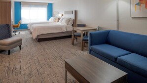 A hotel room with a bed, a blue sofa, a wooden coffee table, a desk, and a chair.