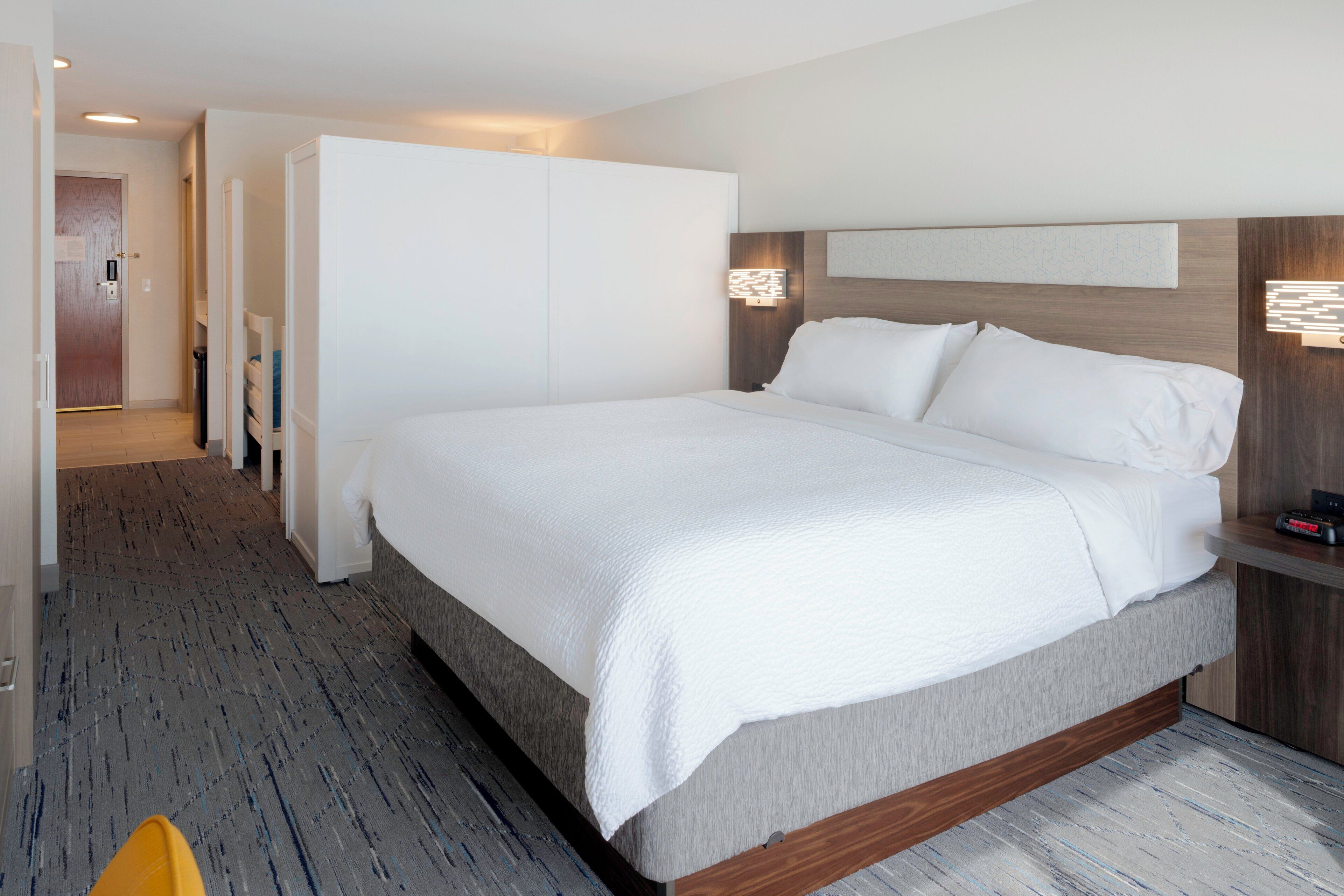 Moderni hotellihuone, jossa on suuri sänky, vaatekaappi ja yöpöytä.