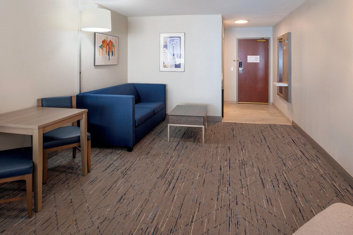 A room with a blue sofa, a wooden table, a small grey table, and a patterned carpet.