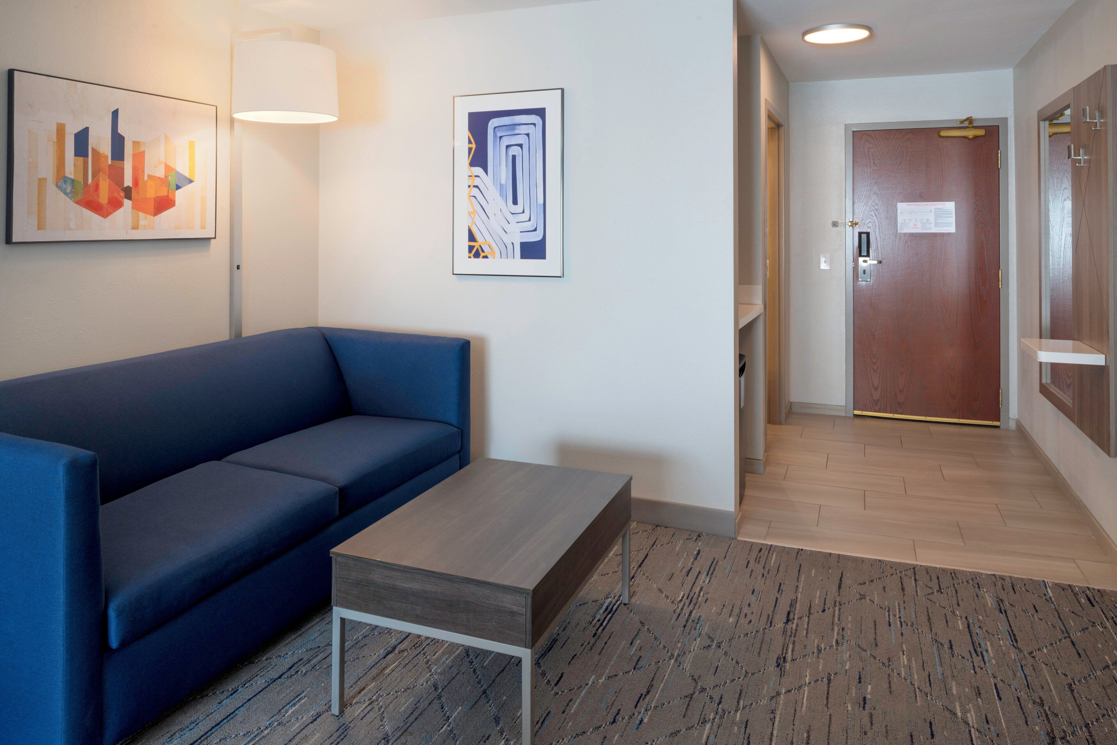 Un hall d’hôtel moderne avec un canapé bleu, une table basse en bois et deux tableaux abstraits accrochés au mur.