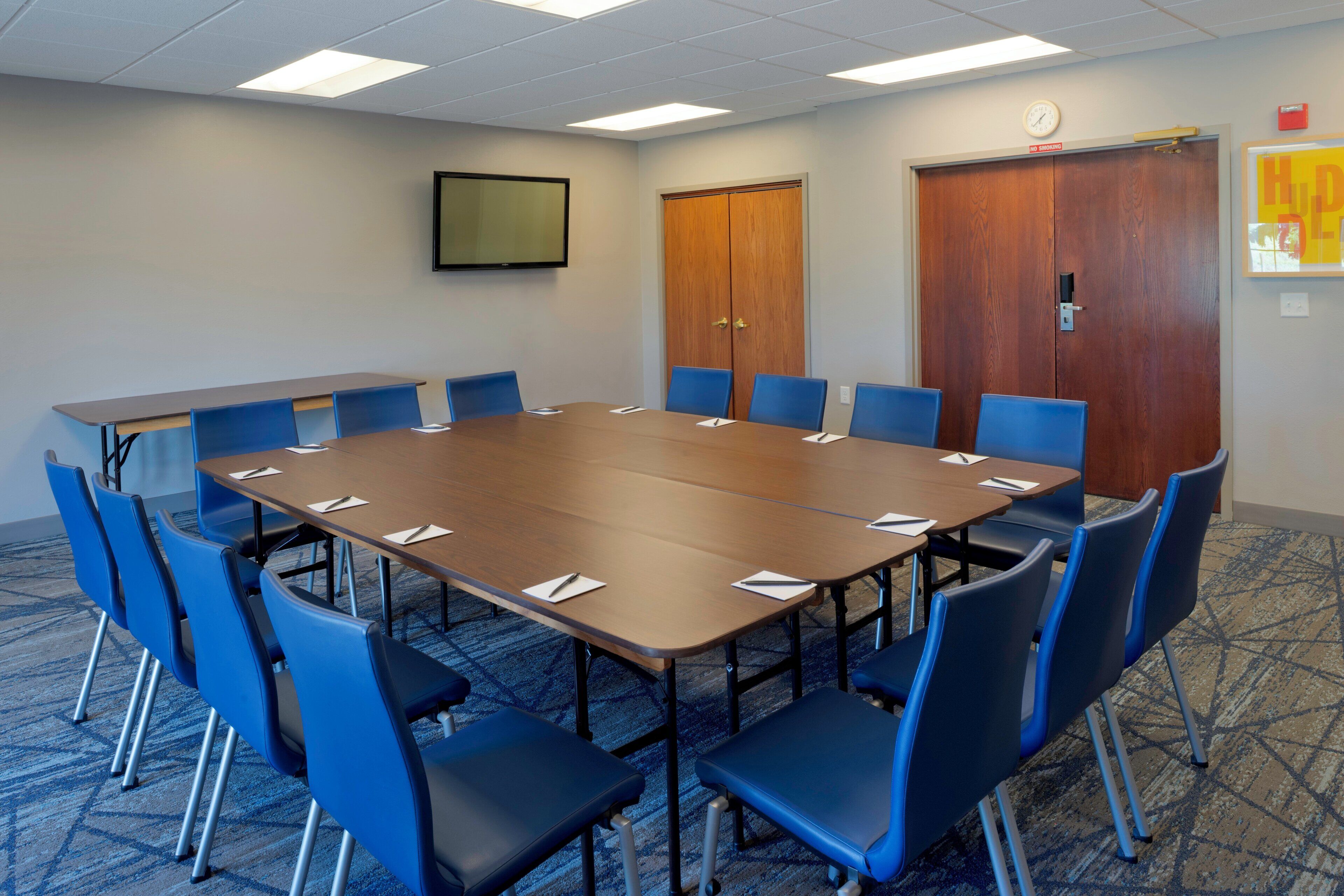 A conference room with a large table, blue chairs, a clock, and a door.