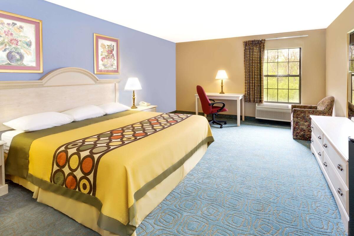 A hotel room with a bed, two chairs, a desk, and a dresser.