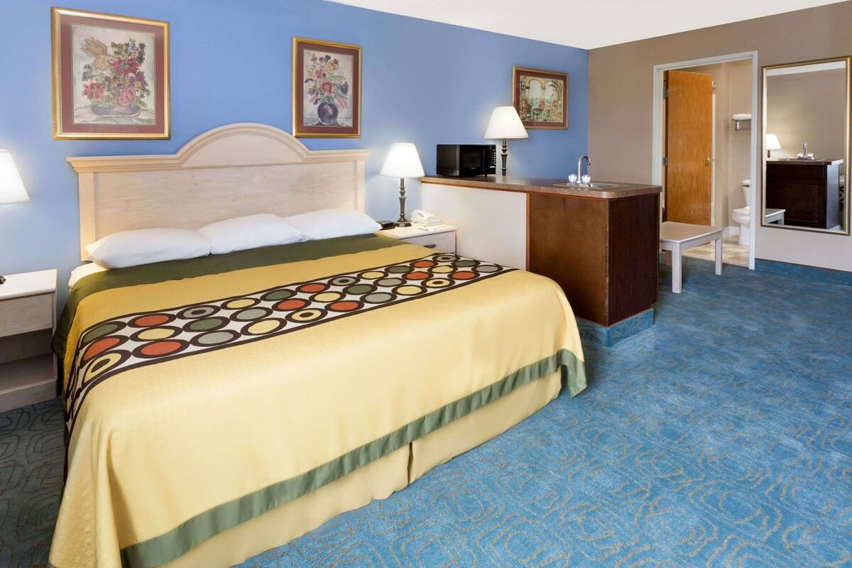 A hotel room with a bed, bedside tables, a desk, a mirror, and artwork on the walls.