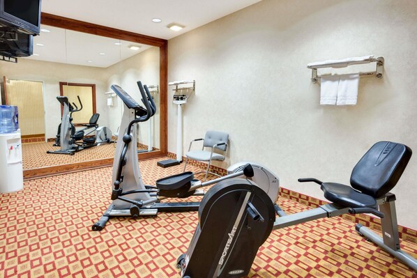 A hotel gym with exercise equipment, a mirror, and a towel rack.