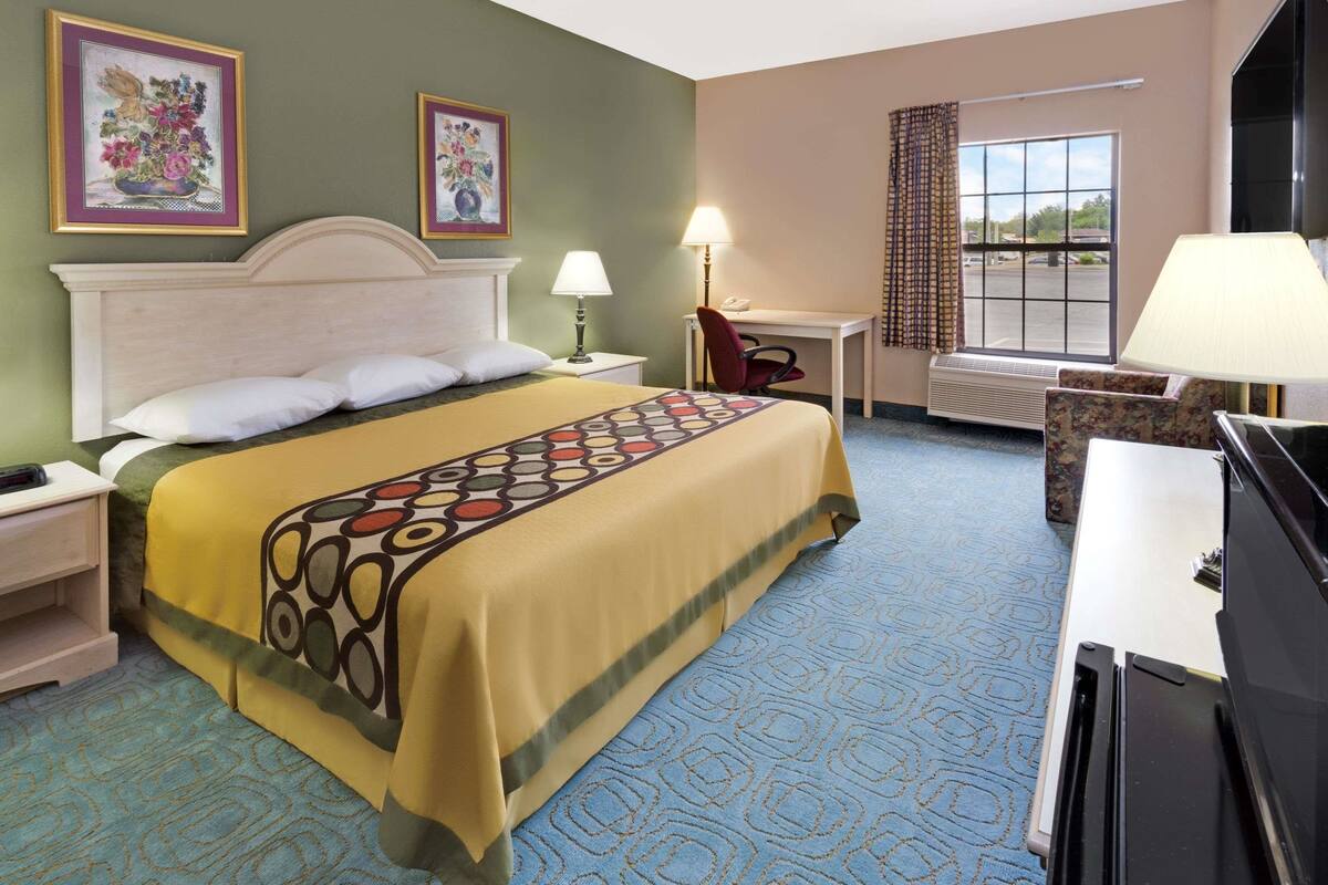 A hotel room with a bed, a desk, a chair, a TV, and a window with curtains.