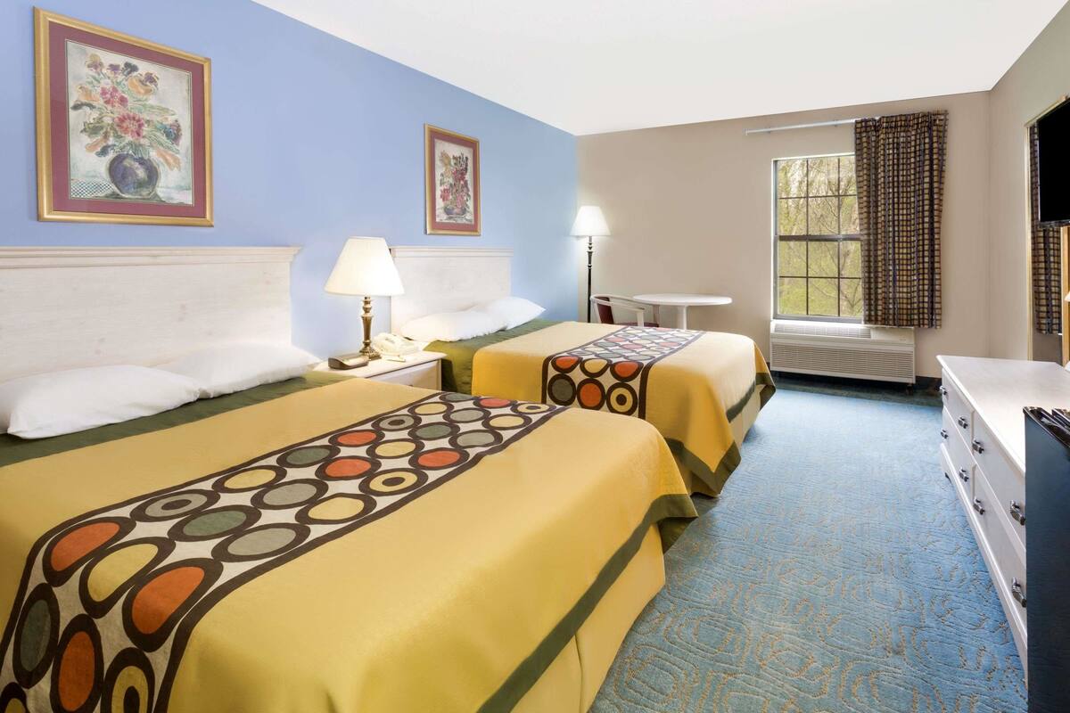 A hotel room with two beds, a desk, a chair, a window with curtains, and a flat-screen TV.