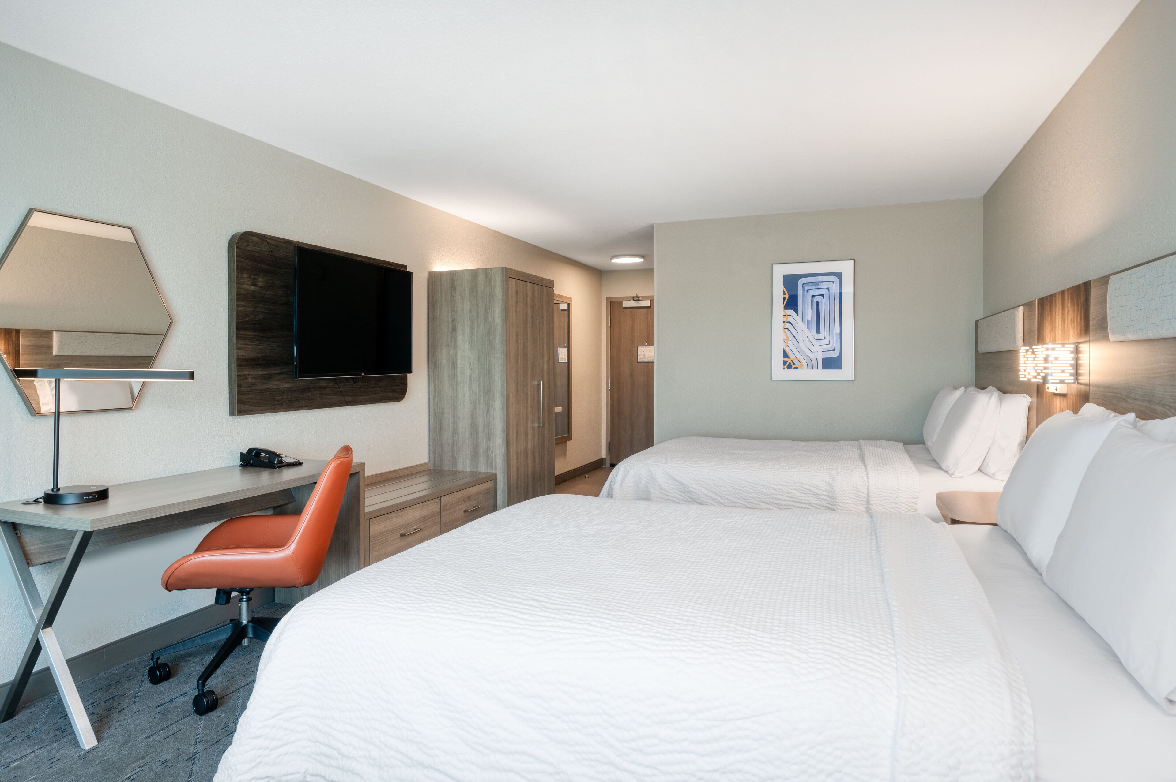 Une chambre d’hôtel avec deux lits, un bureau avec une chaise, une télévision et un tableau au mur.