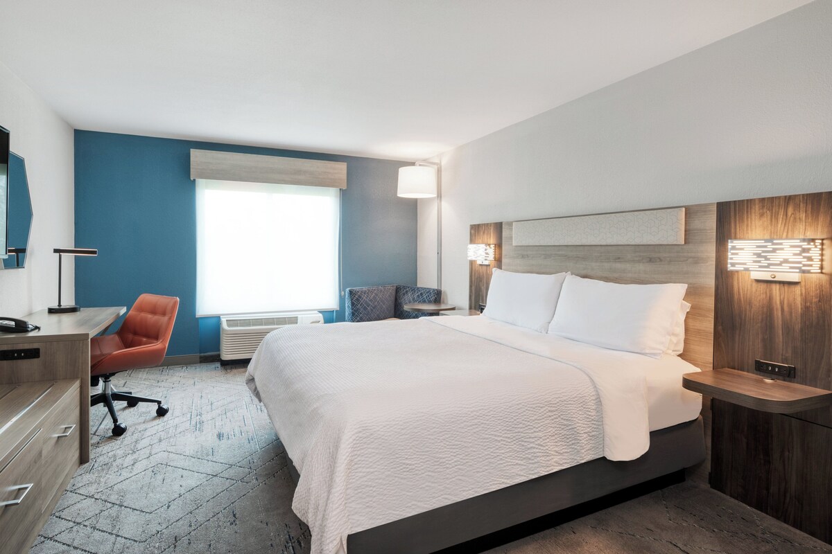 A modern hotel room with a large bed, a desk, and a chair.