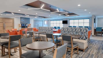 Un moderno vestíbulo de hotel con zonas de estar, una estación de café y un amplio ventanal que proporciona luz natural.