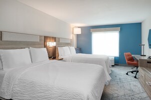 Habitación de hotel con dos camas, un escritorio, una silla y un ventanal grande.