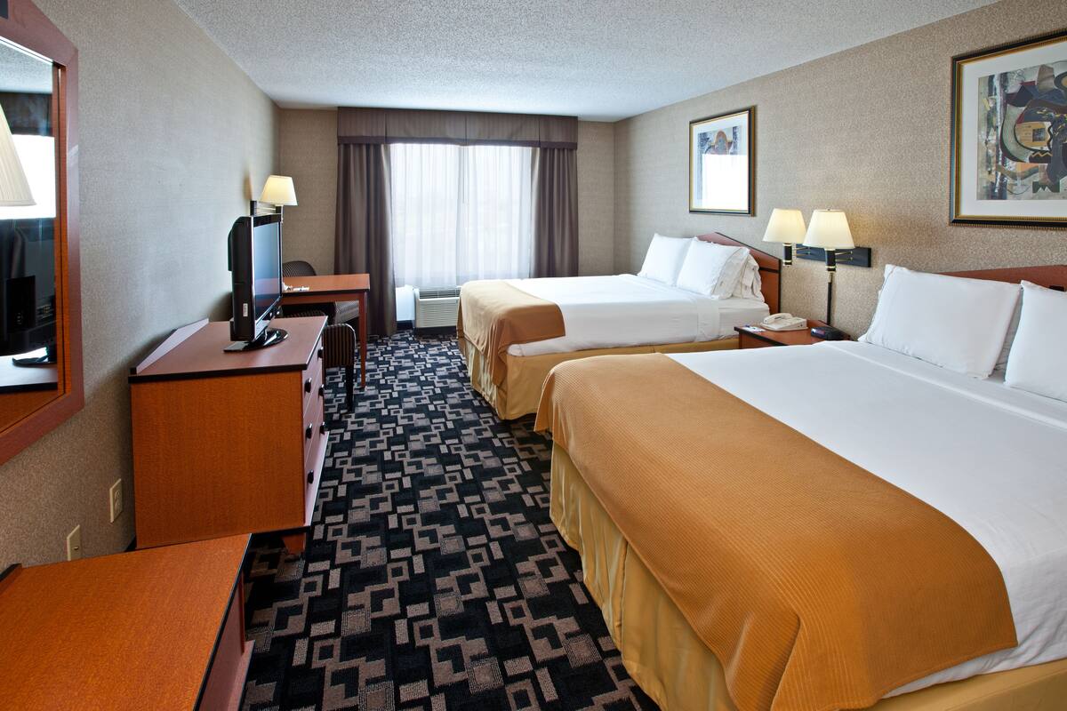 Ein Hotelzimmer mit zwei Betten, einem Schreibtisch mit Computer, einem Stuhl, einem Fernseher und einem Fenster mit Vorhängen.