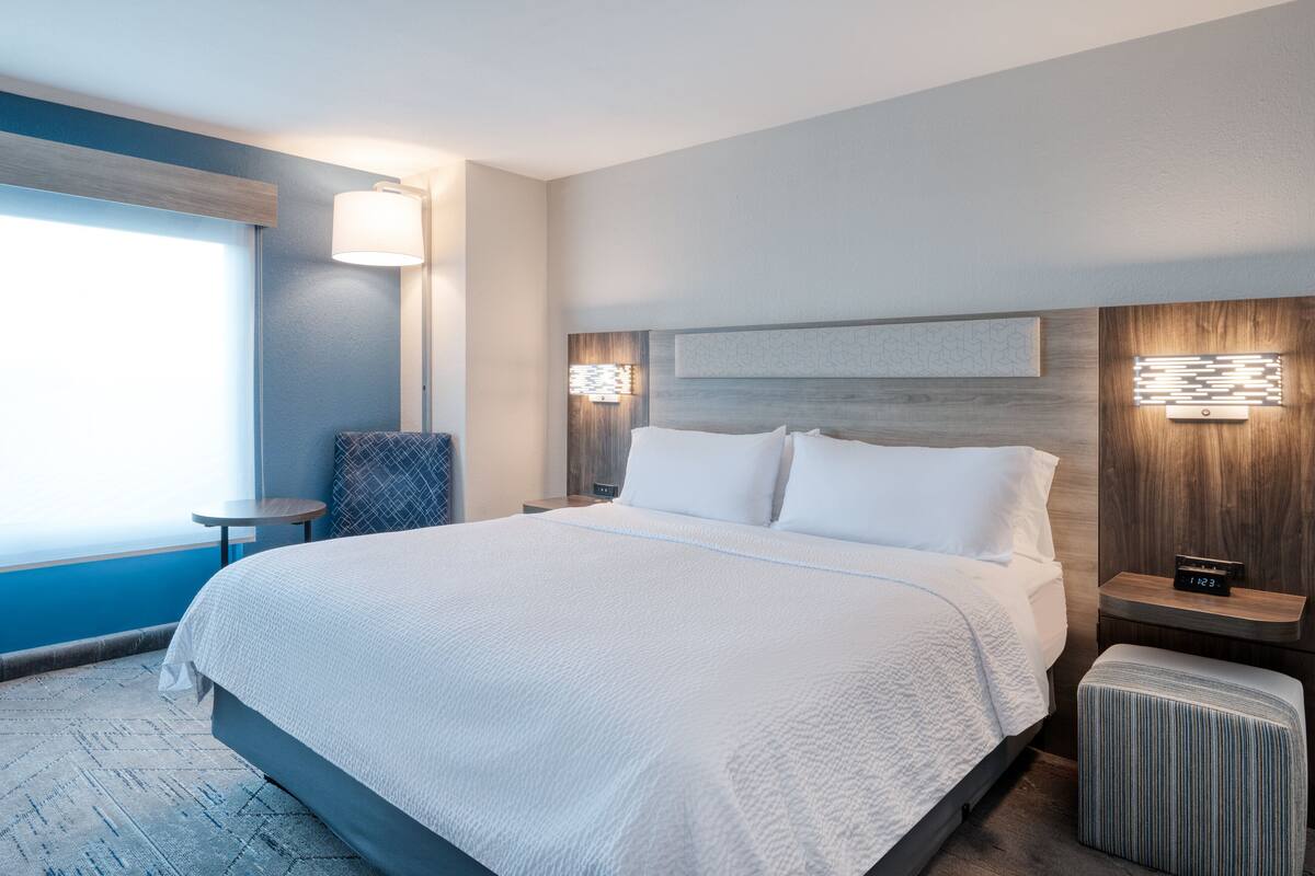 Ein modernes Hotelzimmer mit einem großen Bett, Nachttischen, einem kleinen runden Tisch und einem Sessel.