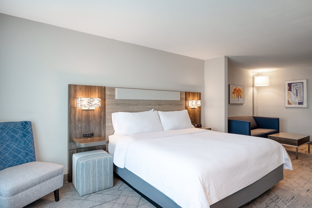 Ein modernes Hotelzimmer mit einem großen Bett, einem Nachttisch, einem Sessel und einem kleinen Schreibtisch.