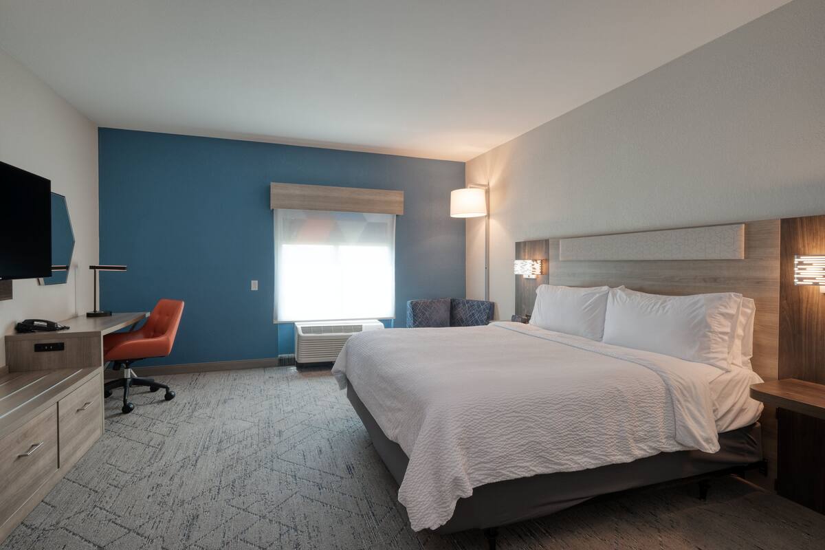 Ein Hotelzimmer mit Bett, Schreibtisch, Stuhl, Fernseher und einem Fenster mit Jalousien.