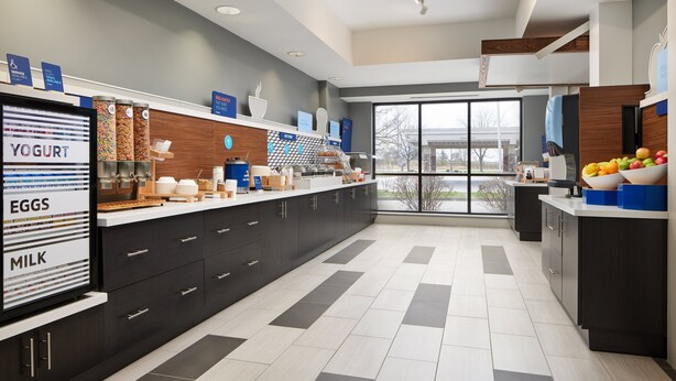 A modern kitchen with a large island, labeled sections for yogurt, eggs, and milk, and a view through large windows. - Holiday Inn Express Hotel & Suites Greenwood by IHG (Greenwood)