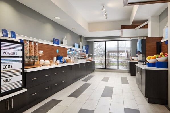 A modern kitchen with a large island, labeled sections for yogurt, eggs, and milk, and a view through large windows. - Holiday Inn Express Hotel & Suites Greenwood by IHG (Greenwood)