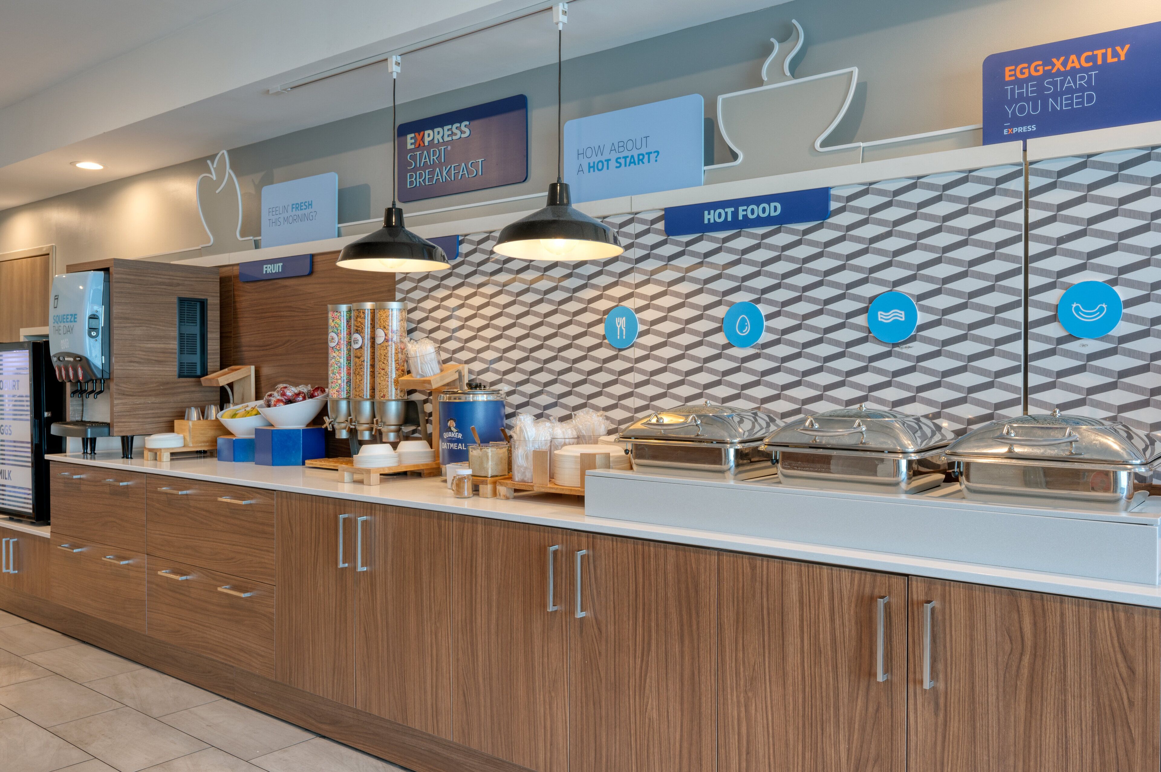 A modern breakfast bar with a geometric patterned wall, a sign for 'Express Start Breakfast', and various food service items.