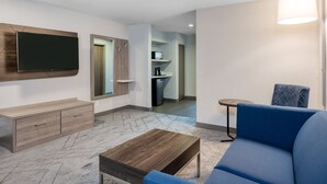 A modern living room with a flat-screen TV, a sofa, a coffee table, and a small side table. - Holiday Inn Express Hotel & Suites Greenwood by IHG (Greenwood)