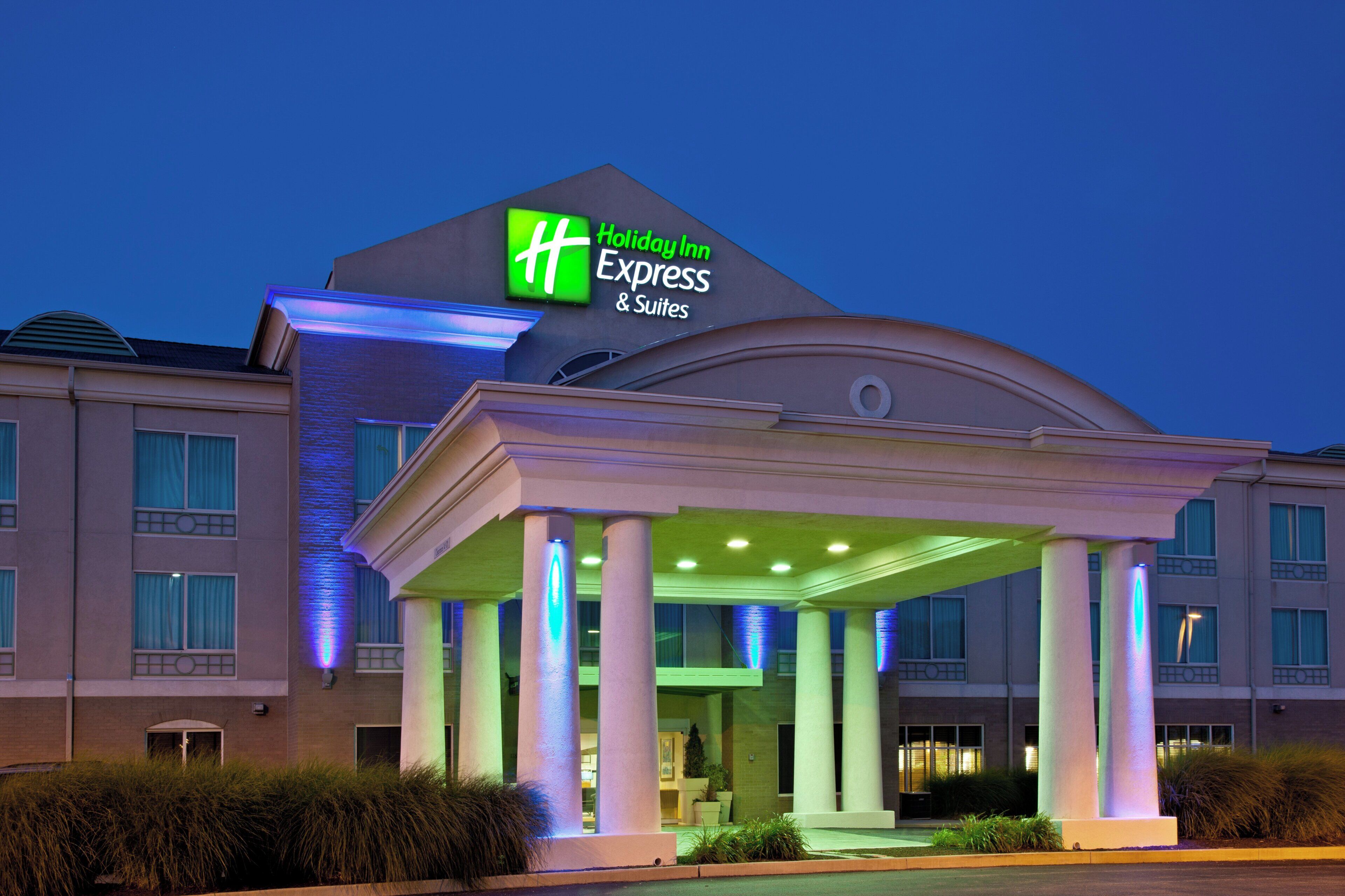 A Holiday Inn Express & Suites hotel with a prominent sign, a covered entrance, and a landscaped front yard.
