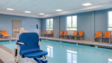 A pool area with blue and orange chairs, a blue chair with a safety bar, and a door in the background.
